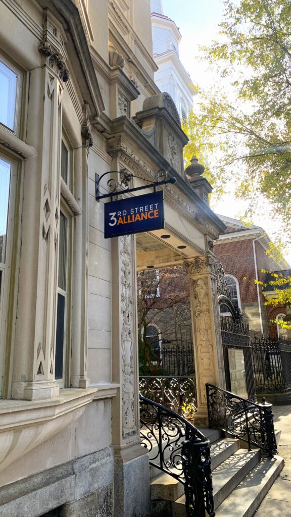 A blade sign of the Third Street Alliance logo hanging off of the front of the Third Street Alliance building.